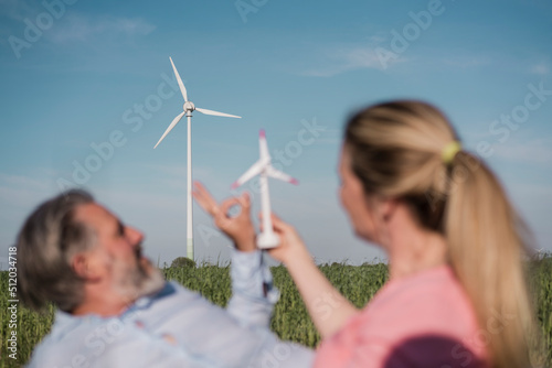 Woman holding windm turbine model sitting with man in field photo