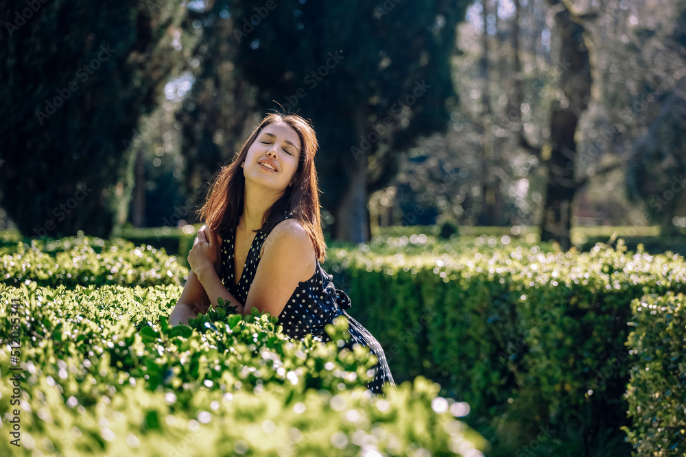 Woman with eyes closed leaning on hedge in garden on sunny day Woman with eyes closed leaning on hedge in garden on sunny day