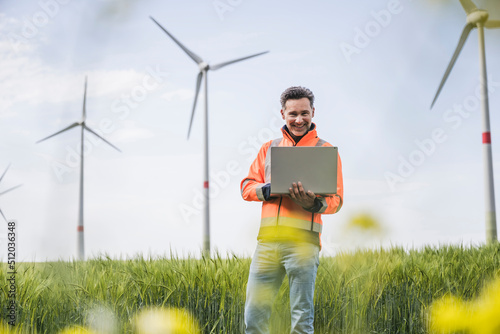 Happy engineer with laptop standing on field photo