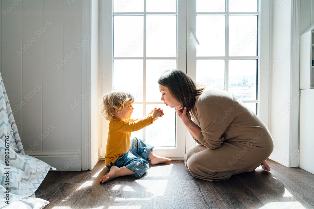 © Westend61 - Happy son playing with mother sitting by window at home © Westend61 - Happy son playing with mother sitting by window at home
