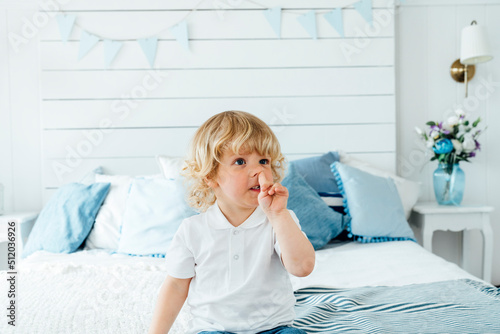 Boy picking nose sitting on bed at home
