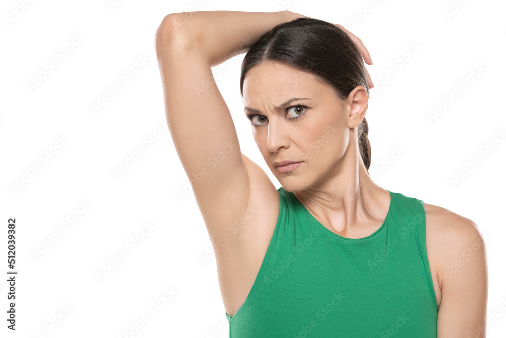 A young worried woman smells her underarm. on a white background A young worried woman smells her underarm. on a white background