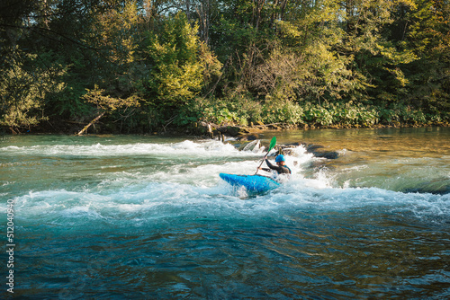 Young teenager cruising down whitewater rapids in a blue kayak, beautiful river nature on a sunny summer day, handheld shot.