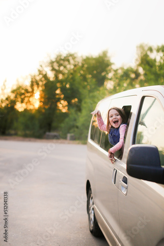Funny European kid girl peeking out of window of minivan, family trips with children © natalialeb