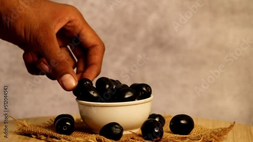 Man eating jamun fruit on white bowl with dark background, blueberries picking on hand, berry pick up man