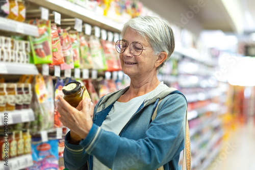 Obraz na płótnie Portrait smiling senior woman making purchases in the supermarket selecting some jam
