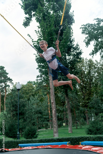 Happy boy bungee jumping in trampoline. Teenager in an amusement park is having fun. Weekend at theme park. Vertical frame.