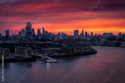The illuminated london skyline with river Thames and skyscrapers during a fiery summer sunset, England