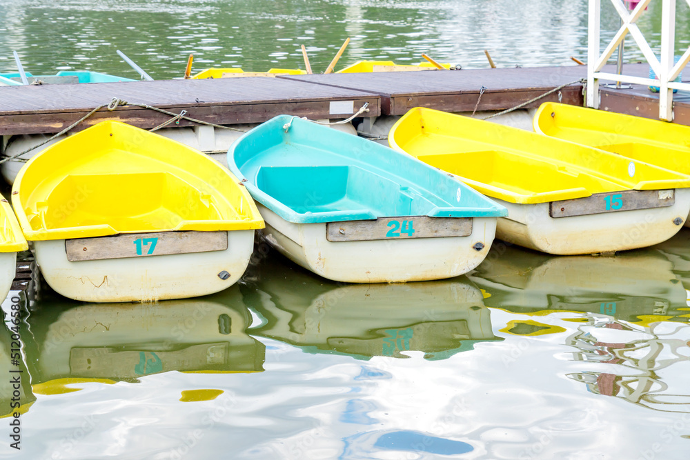 Obraz premium Row of blue and yellow boats parked at the pier of the lake. boat station. Tourist resort on the coast of river