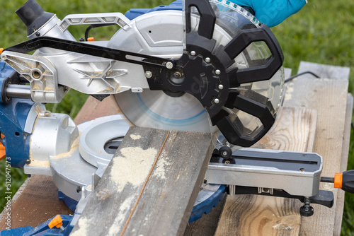 The worker saws the boards. Sawmill. timber harvesting process. Miter saw for cutting wood at work. Tool for carpentry. A man works with a tool. Partial view of joiner's boards with miter saw.