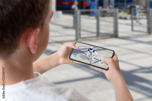 Boy programs and controls the robot on the street via augmented reality technology concept photo