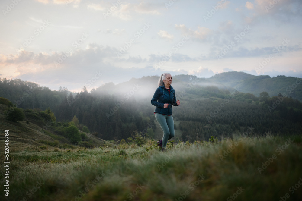 Senior woman jogging in nature on early morning with fog and mountains in background.