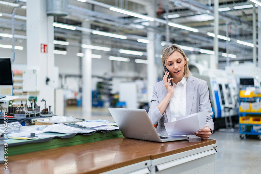 Businesswoman with laptop on the phone in factory Businesswoman with laptop on the phone in factory