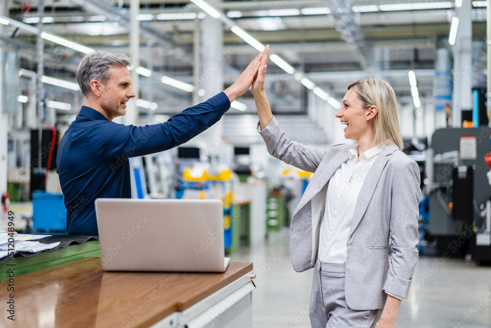 Happy businessman and businesswoman high fiving in factory Happy businessman and businesswoman high fiving in factory