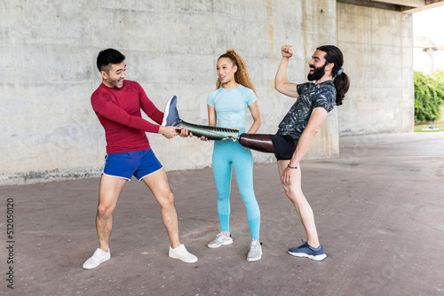 man with amputated leg, shows his prosthesis to his friends, multiracial, having fun with prosthesis in his hand. sport concept