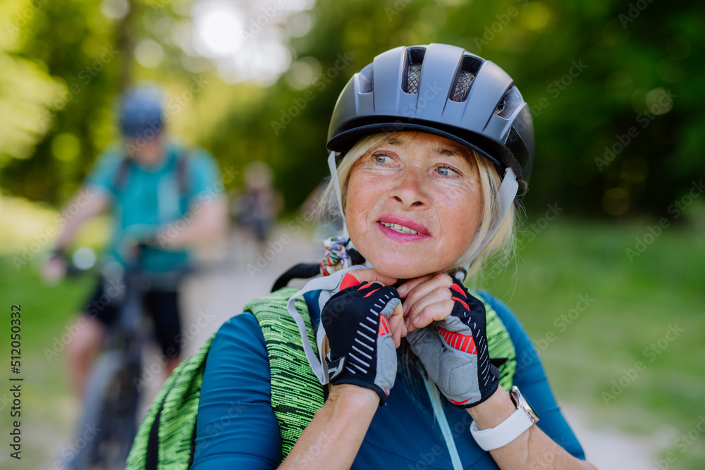 Active senior couple riding bicycles at summer park, woman is putting on helmet, healthy lifestyle concept. Active senior couple riding bicycles at summer park, woman is putting on helmet, healthy lifestyle concept.
