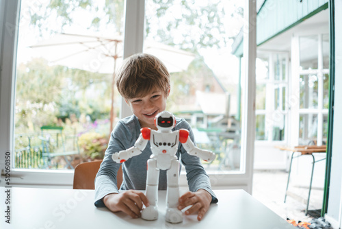 Happy boy with toy robot sitting at table photo