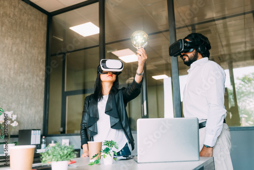 Businesswoman wearing VR glasses and examining light bulb by colleague photo