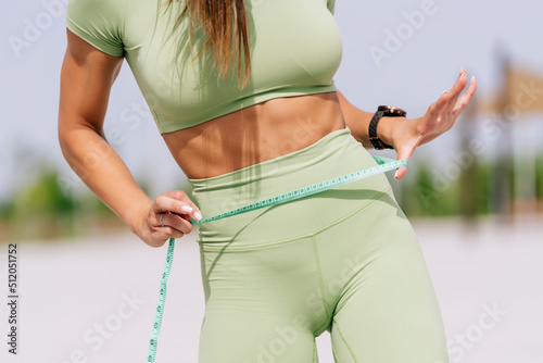 Hands of woman measuring waistline on sunny day