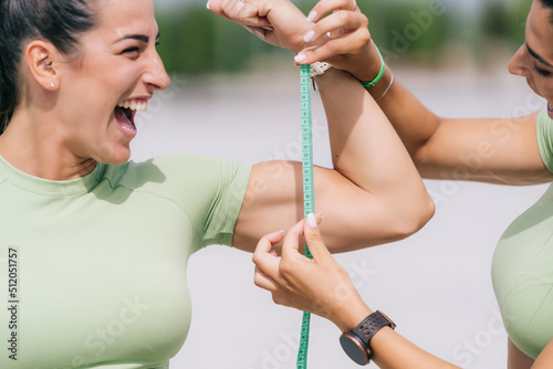 Happy woman measuring sister's bicep on sunny day photo