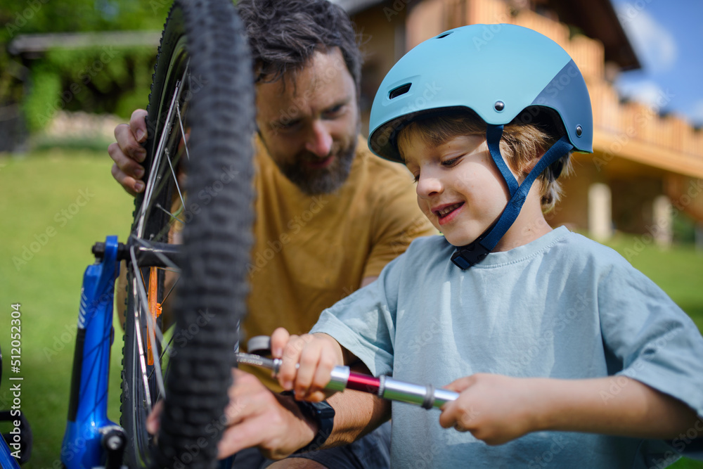 Father with little son together preparing bicycle for a ride, pumping up tyres in garden in front of house.