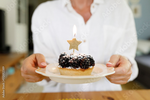 Woman holding plate of blackberry tart with lit candle at home photo