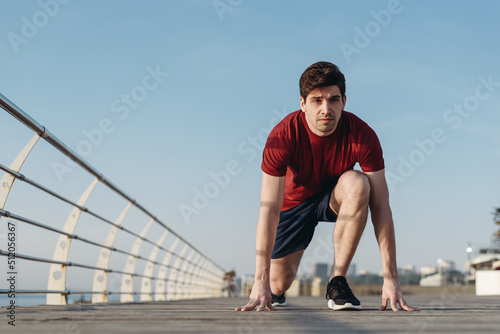 Full body young strong sporty toned fit sportsman man 20s wear sports clothes stand at low start going to run warm up training at sunrise sun dawn over sea beach outdoor on pier seaside in morning © ViDi Studio
