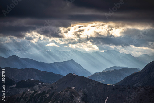 Sun rays filter between black clouds at sunset, Stelvio Mountain pass, Stelvio National Park, Valtellina, Lombardy, Italy photo