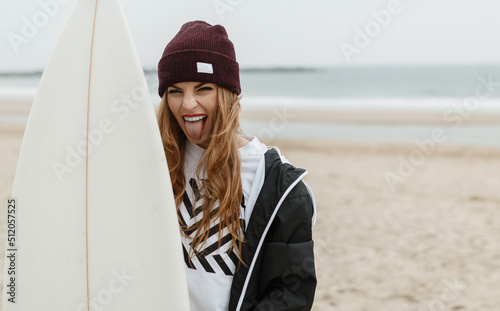 Girl with hat and surfboard sticks out her tongue