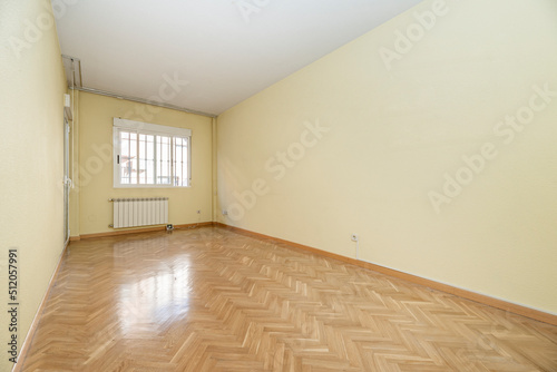 Empty living room in a house with herringbone oak parquet, wooden carpentry and white aluminum window with radiator below and light yellow painted walls © Toyakisfoto.photos