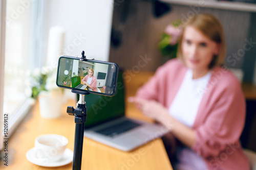 Selective focus of woman blogger broadcasts live on phone at home next to laptop