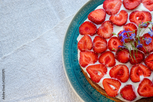 Cake with strawberries and cream on blue plate. Summer Strawberry and Cream sponge Layer Cake on white table cloth background. Top view, copy space. Midsummer food dessert