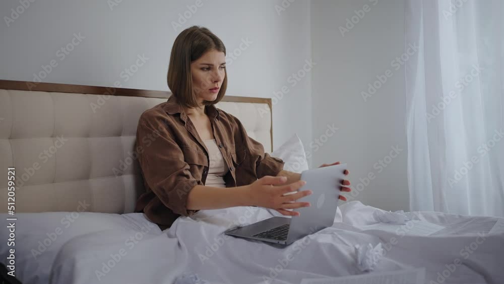 Woman closes laptop and sits with head in hands on bed Woman closes laptop and sits with head in hands on bed
