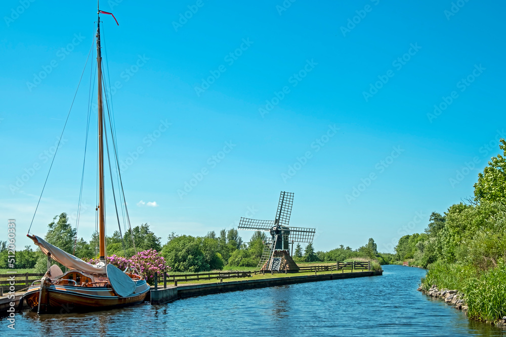Typical dutch landscape, a traditional boat, an old windmill at a canal in Friesland in the Netherlands in spring