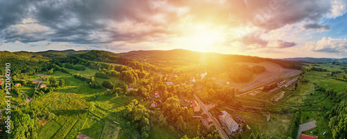 Overhead view of beautiful landscape at sunset, Aerial view of countryside area with village and green fields near mountains, long panorama