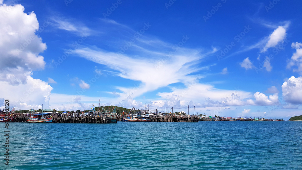 Many fishing boat parked on sea at port near coast and community with blue sky, white clouds and green mountain background and copy space. Landscape of ocean or seascape. Beautiful view and nature 