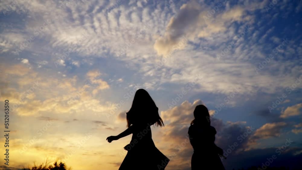 Two young women at a festive disco. Happy girls dancing against the blue sk . Beautiful girls have fun listening to music. Only their dark silhouettes are visible against the sunset sky.