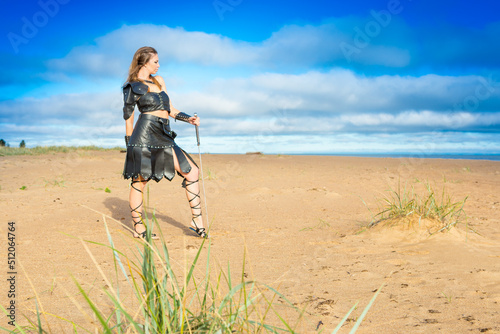 medieval warrioress cosplayer wearing leather plastron, skirt, vambrace and brassard with two-handed sword is walking along the marge photo