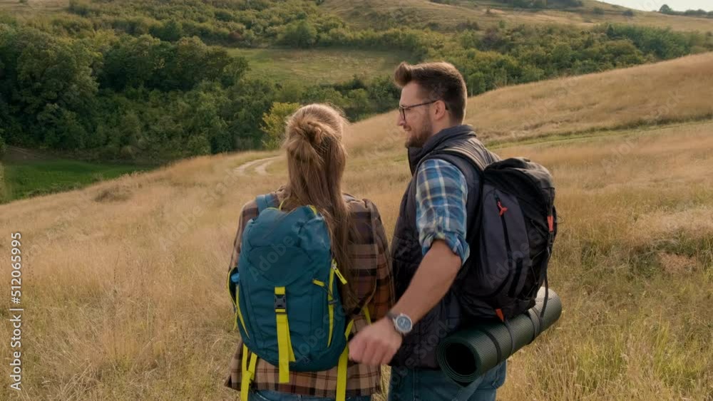 Rear view of couple with backpacks hiking together in nature on autumn day.