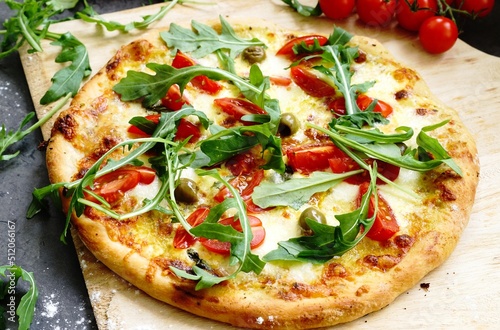 Freshly baked pizza with arugula, tomato, olive,  hollandaise sauce and mozzarella