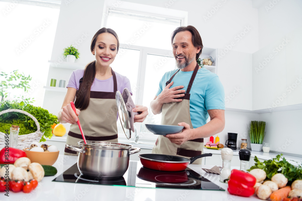 Photo of charming positive mature wife husband dressed aprons boiling pasta cooking lunch indoors home room Photo of charming positive mature wife husband dressed aprons boiling pasta cooking lunch indoors home room