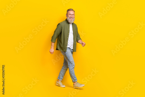 Full length profile portrait of cheerful aged man walking have good mood isolated on yellow color background