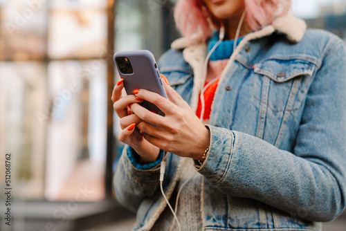 Young white woman in earphones using cellphone at street