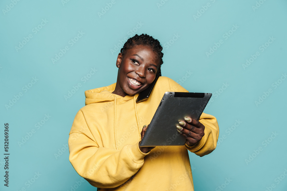 Young black woman talking on cellphone while using tablet computer Young black woman talking on cellphone while using tablet computer