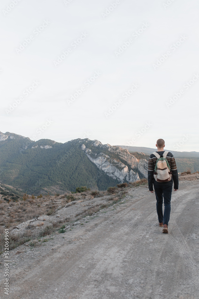 Shaved guy with a backpack walks along a path in the middle of mountains