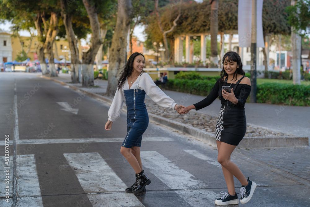 Women holding hands while crossing the street and using a mobile