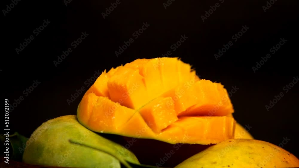a mango rotating on the turntable. Juicy sliced, hedgehog style served mango, isolated on the black background