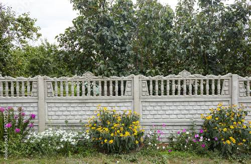 An old classic balustrade outdoors with flowers. Antique-like stone fence with colums near European suburban cottage