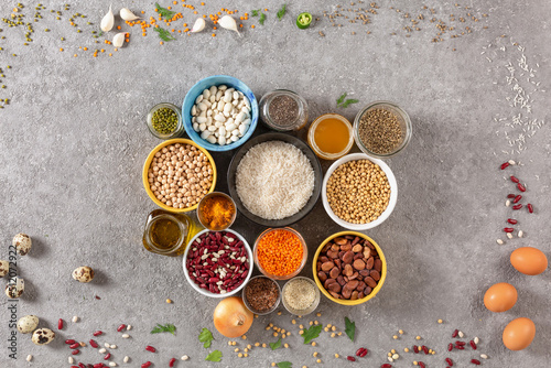 Concept of vegetarian food and diet on gray concrete background, legumes, seeds and cereals in colored bowls grouped with copy space