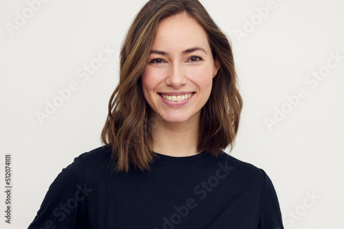 Portrait of beautiful natural brunette woman, smiling and looking in camera with white teeth. Close-up portrait of cute female girl in black t-shirt isolated on white background. © Martin Villadsen